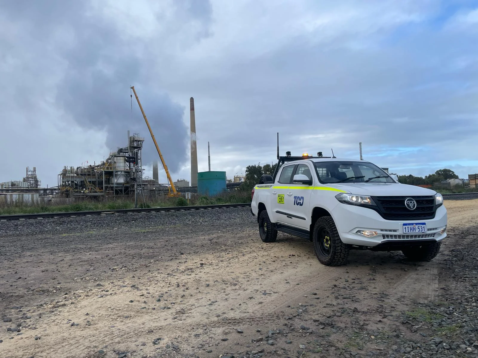 White Tembo Tusker with hi-vis striping and a roof light bar parked on gravel beside a rail line at an industrial plant
