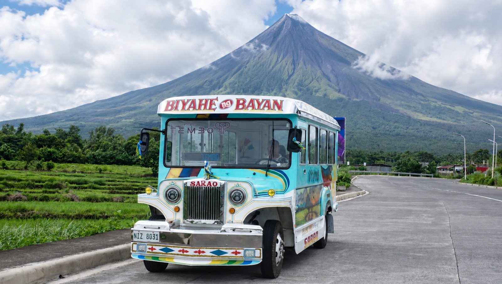 Electric Sarao jeepney on the road with Mayon Volcano behind